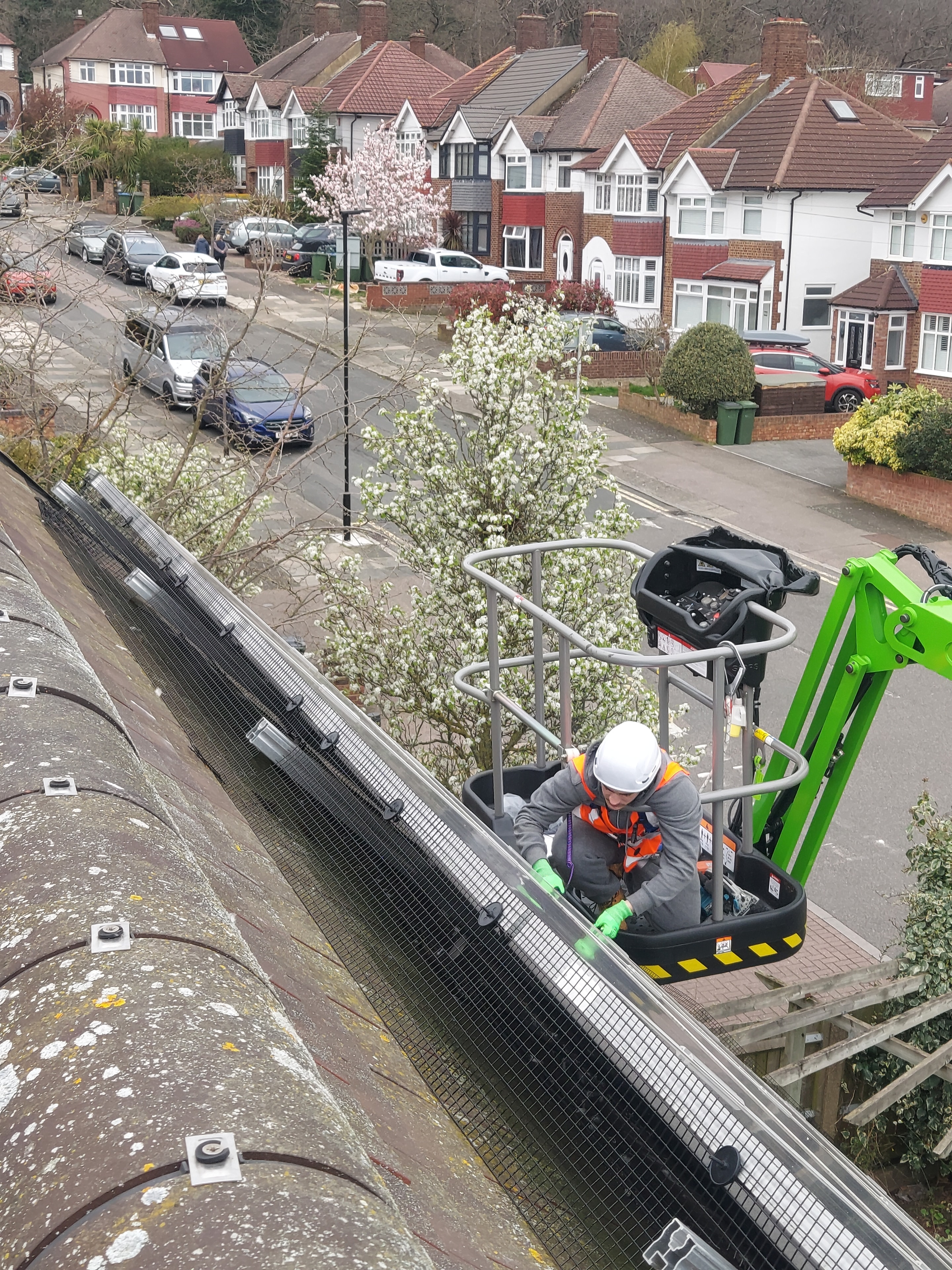 Worker installing bird-proofing mesh on solar panels from a cherry picker